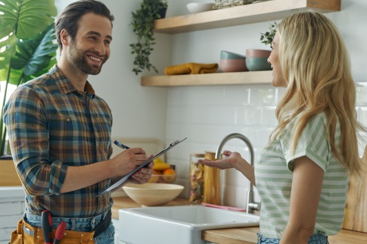 Beautiful young woman talking to male plumber while standing at the kitchen